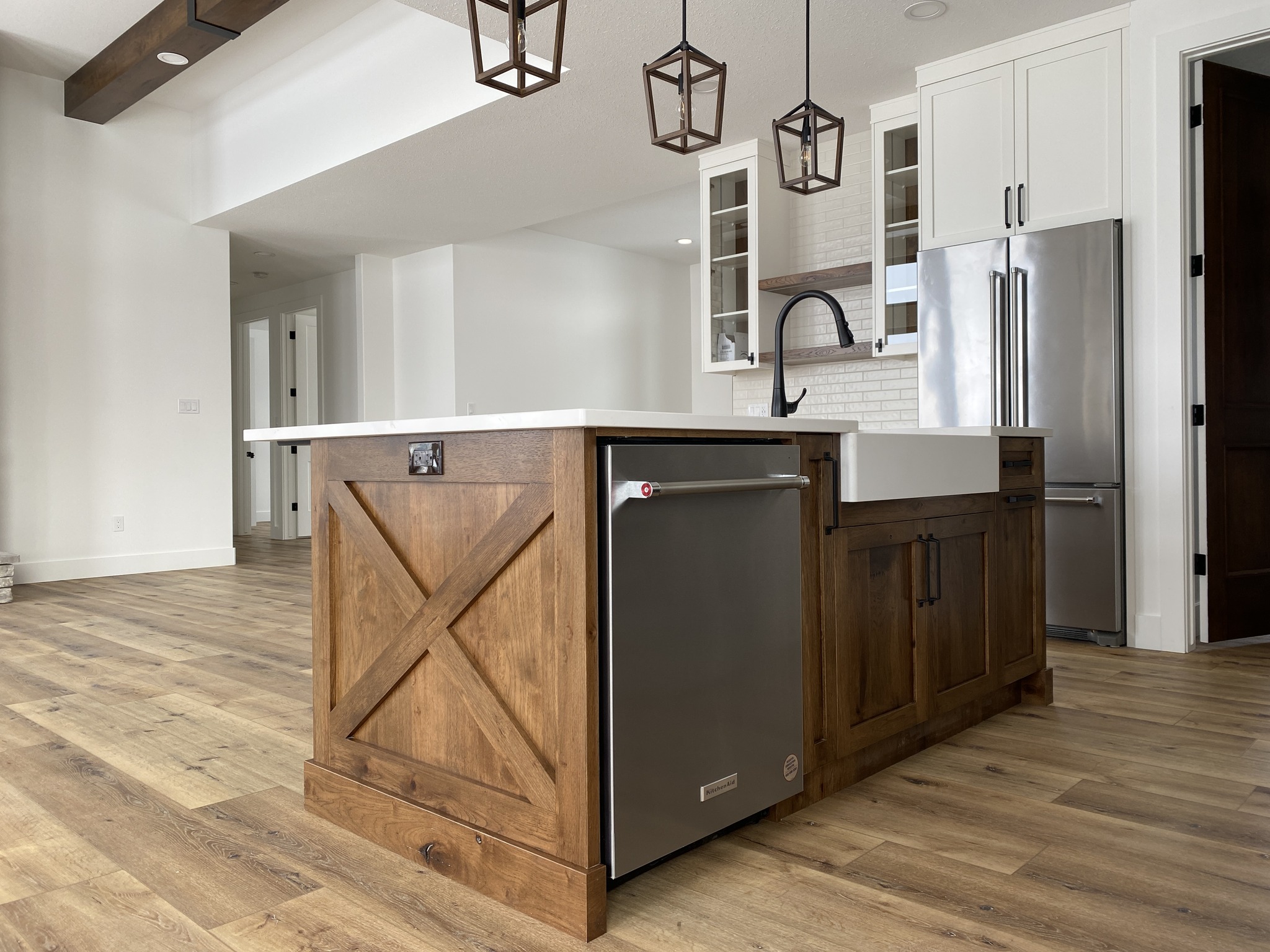 Modern kitchen with wooden island, farmhouse sink, and stainless steel dishwasher. Features open shelving, pendant lights, and wood flooring.