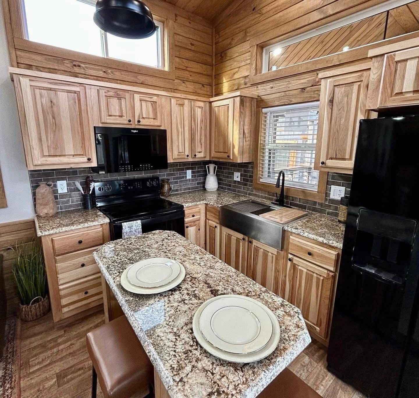 Cozy kitchen with wood cabinets, granite countertops, and an island set for two. Black appliances contrast with natural tones, creating a warm atmosphere.
