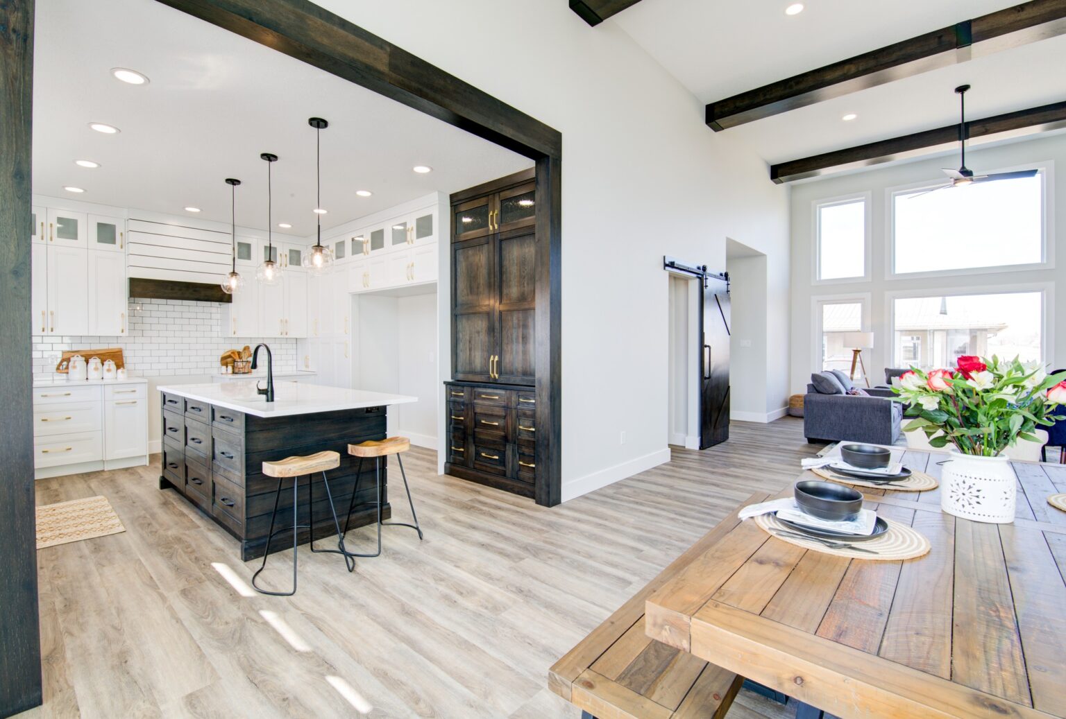 Bright, open-concept kitchen and dining area with white cabinetry, wood accents, and large windows. Inviting ambiance with modern rustic decor.