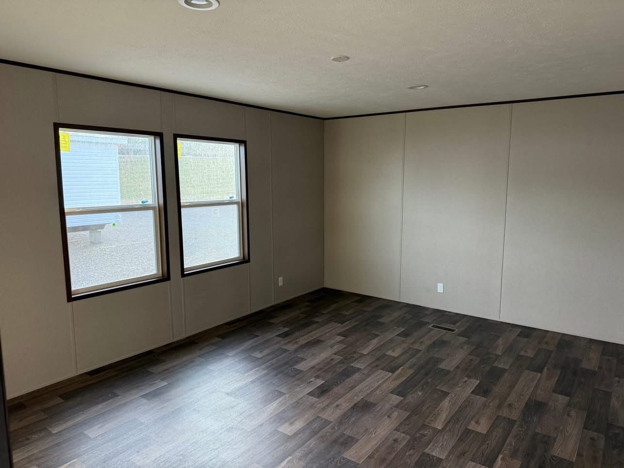 An empty room with neutral-colored walls and two large windows on the left. The floor is dark wood, creating a calm and spacious atmosphere.