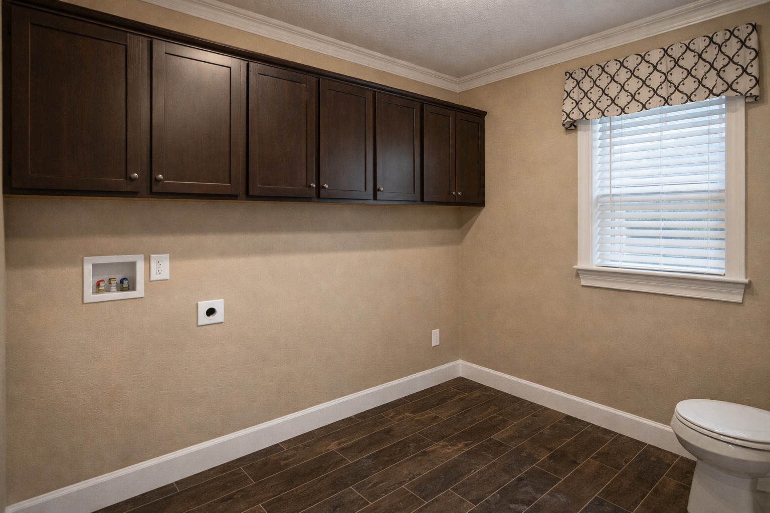 A laundry room with dark wood cabinets, a window with patterned valance, and warm beige walls. It conveys a clean, organized, and functional space.