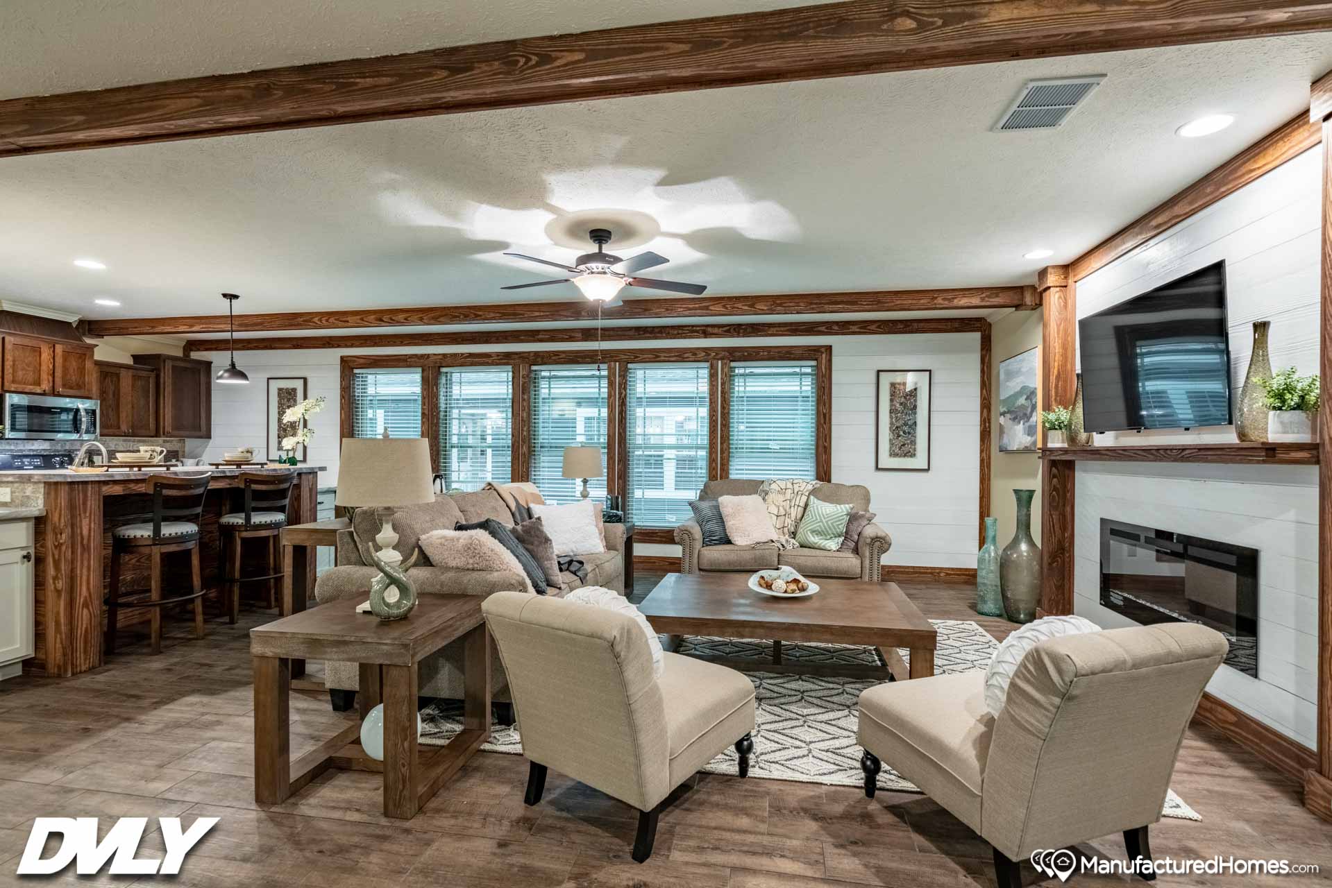 Spacious living room with cozy seating, coffee table, and decor. Features large windows, ceiling fan, wood accents, and warm lighting. Inviting and elegant.