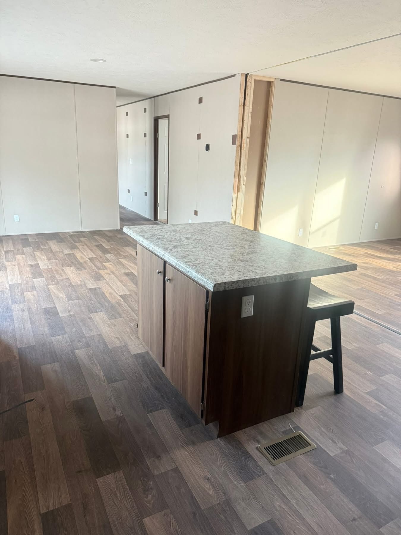 Spacious empty room with light wood flooring and a central kitchen island with granite top and dark cabinets. Soft natural light fills the space, creating an inviting atmosphere.