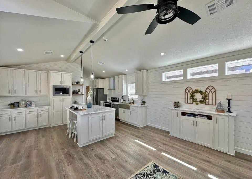 Bright, spacious kitchen with white cabinetry and shiplap walls. Features a center island, modern appliances, and wooden flooring. Cozy, airy vibe.