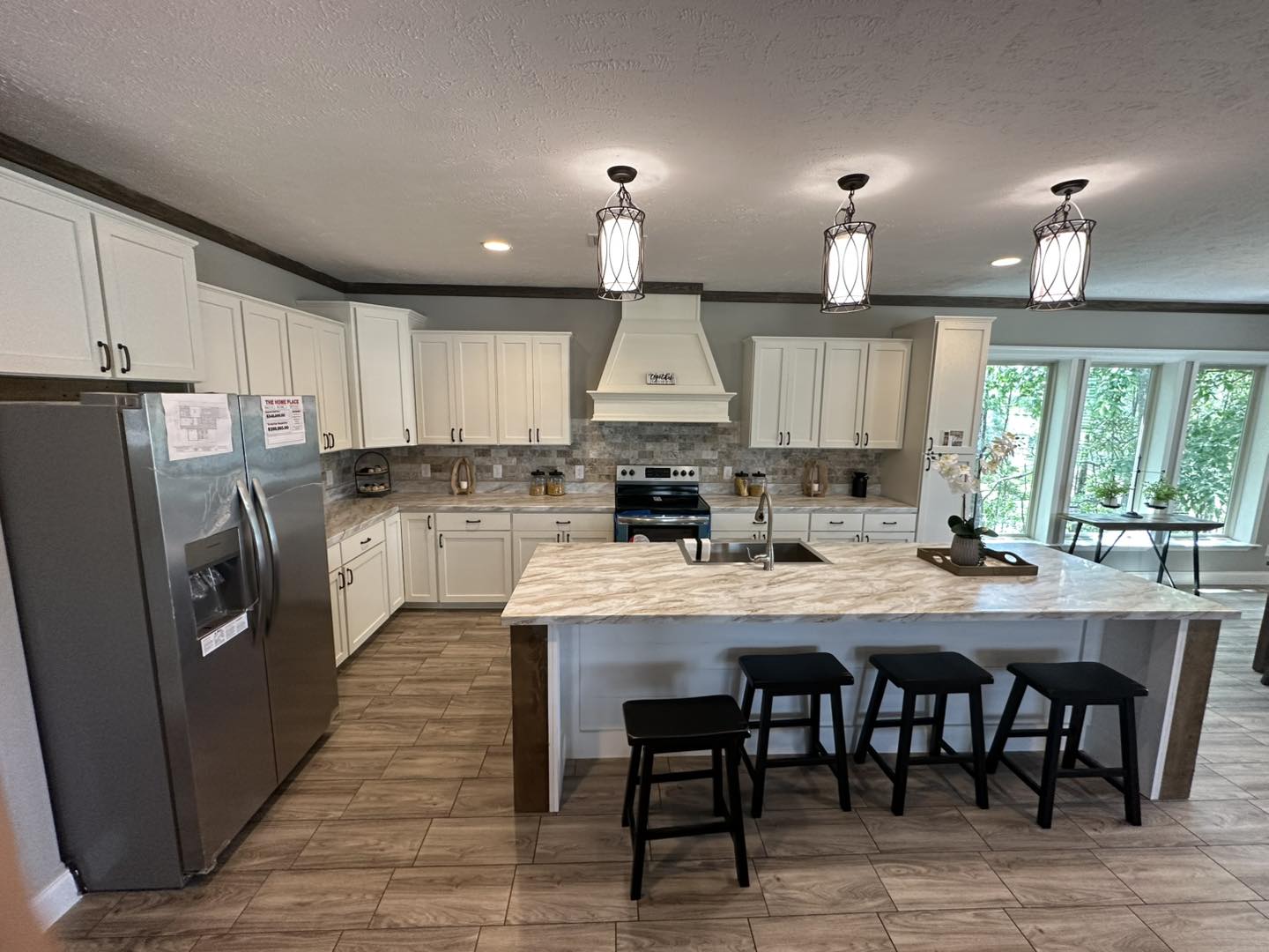 Spacious kitchen with white cabinets, marble island, and black stools. Stainless steel appliances and three pendant lights create a cozy, modern look.