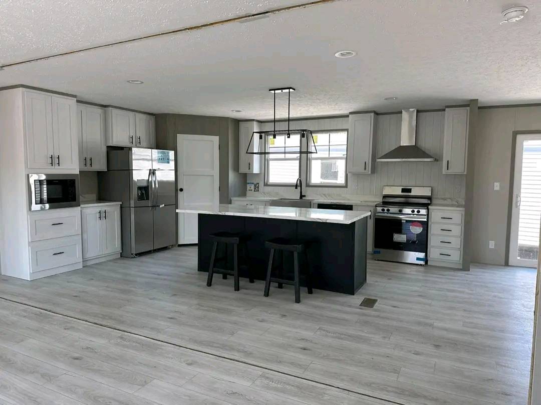 Modern kitchen with light gray flooring, white cabinetry, and stainless steel appliances. Features a central island with two black stools and pendant lighting.