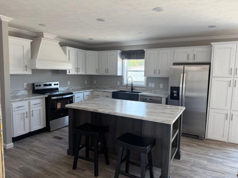 Modern kitchen with white cabinets, stainless steel appliances, and a black farmhouse sink. A central island with two stools adds functionality. Bright and welcoming.