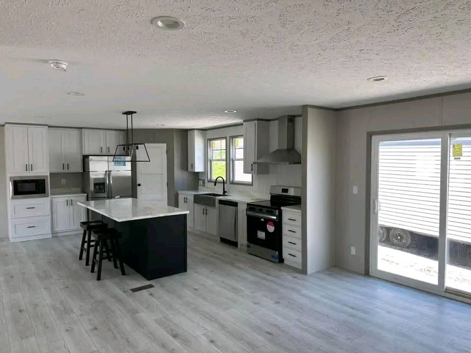 Modern kitchen with white cabinets, stainless steel appliances, an island with bar stools, light wood flooring, large window, and glass doors. Bright and airy ambiance.