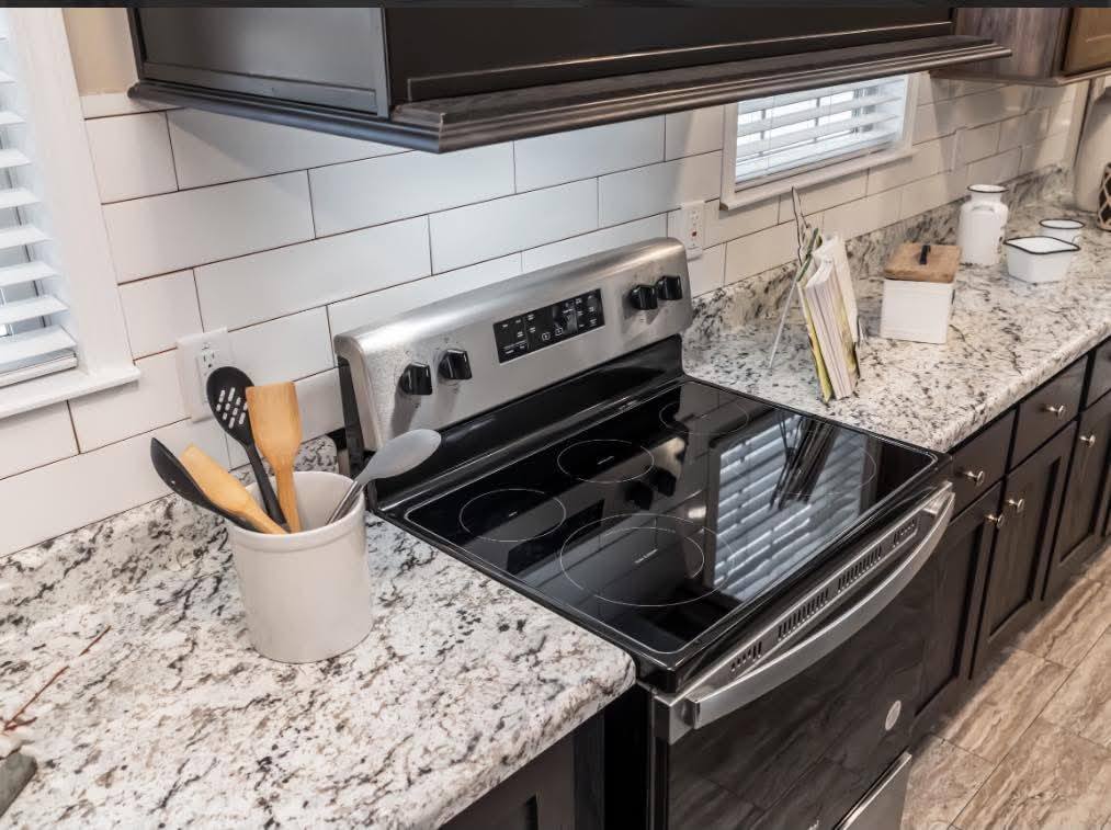 Modern kitchen with black stove, granite countertops, white subway tile backsplash, and a window. Utensils in a holder add a homely touch.