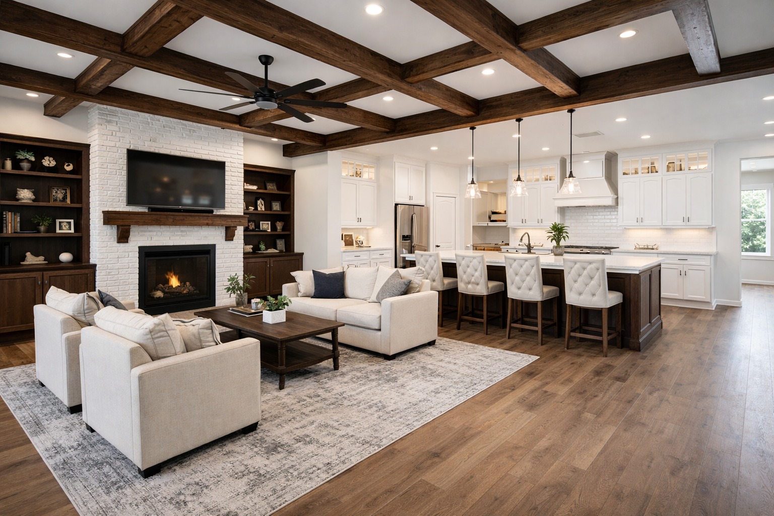 Spacious open-concept living room and kitchen with wooden beams, white walls, cozy beige sofas, a brick fireplace, and island seating under pendant lights.