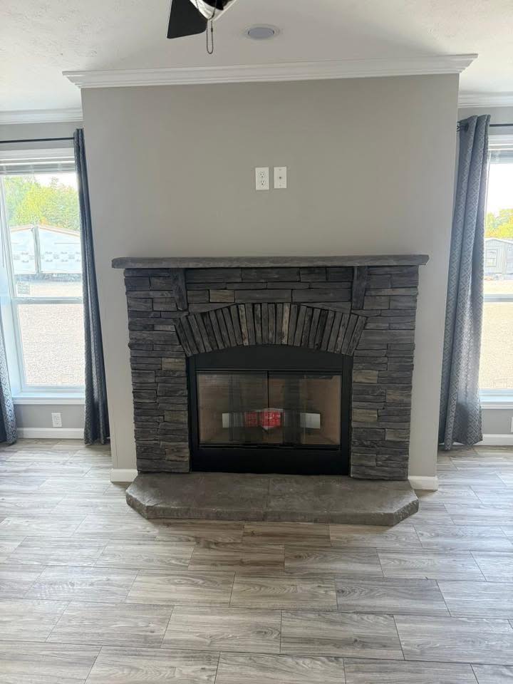 A stone fireplace with a dark wood mantle stands between two windows with blue curtains. The room has light gray walls and wood-like tile flooring.