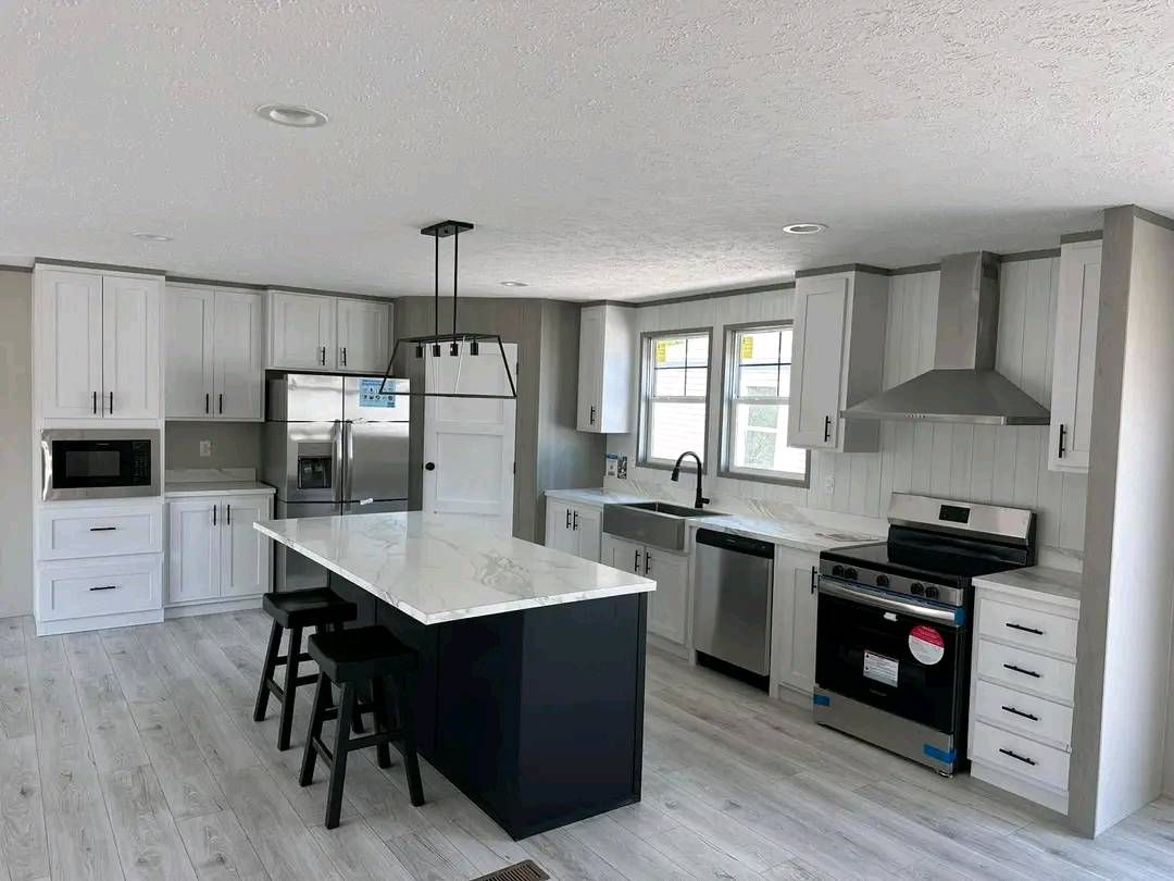 Modern kitchen with white cabinets, dark island, and marble countertops. Stainless steel appliances and light wood flooring create a sleek, fresh ambiance.