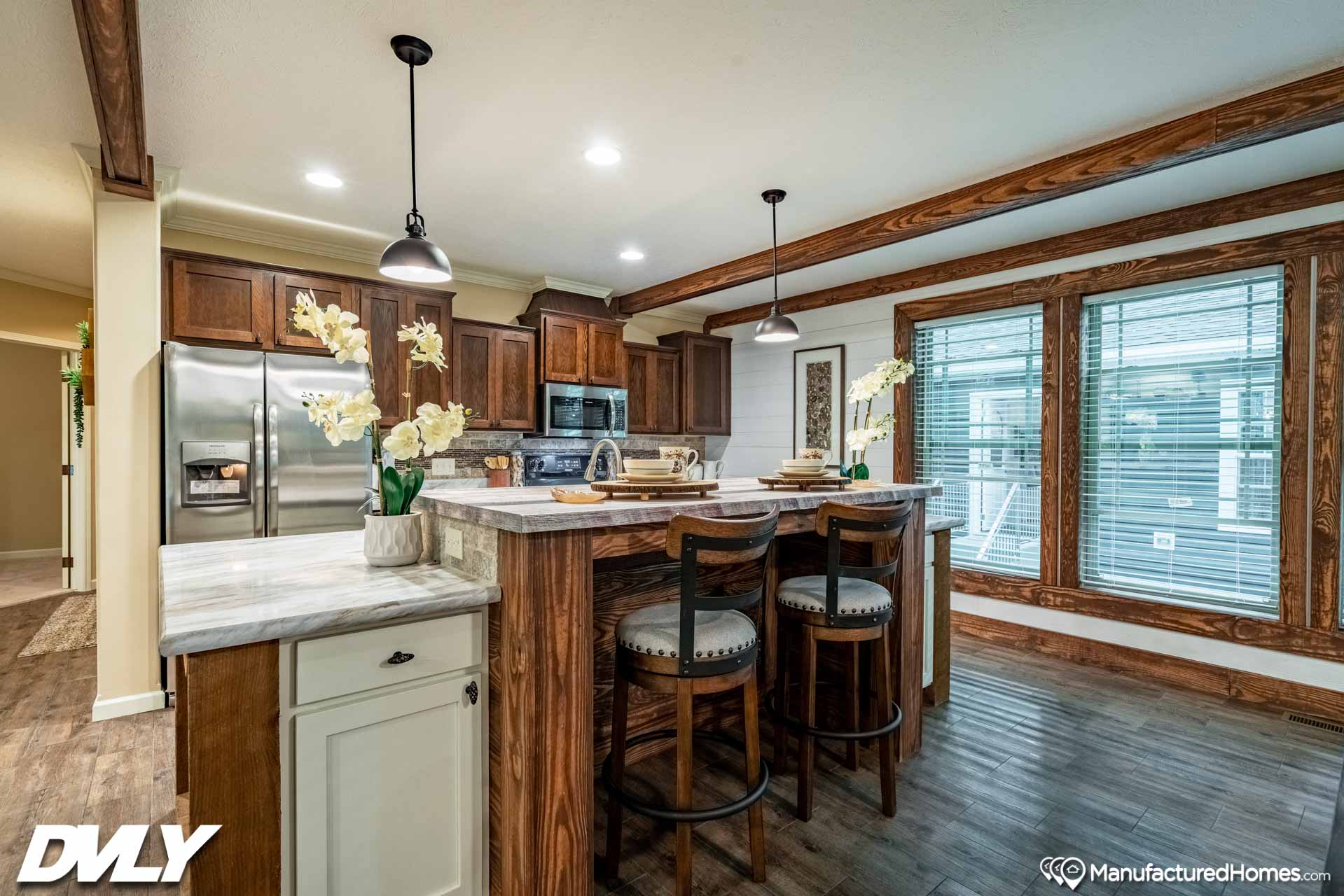 Modern kitchen with a large island featuring bar stools, pendant lights, and wooden cabinetry. Flowers add a fresh touch. Bright and inviting space.