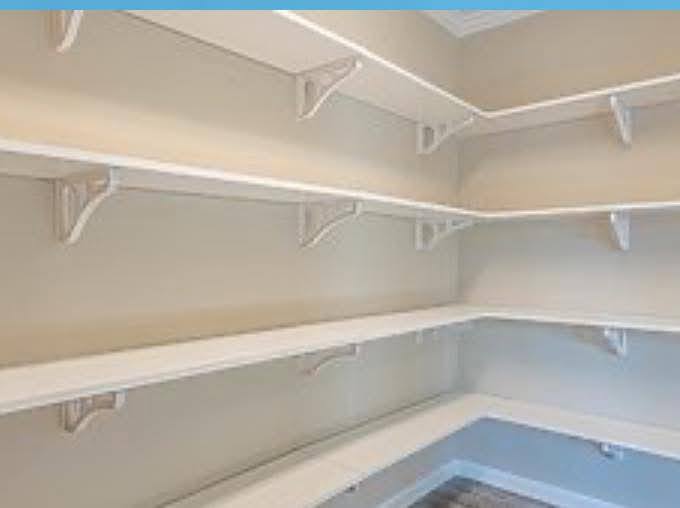Empty pantry with light beige walls and multiple white L-shaped shelves. The bright room has a clean, organized, and spacious appearance.