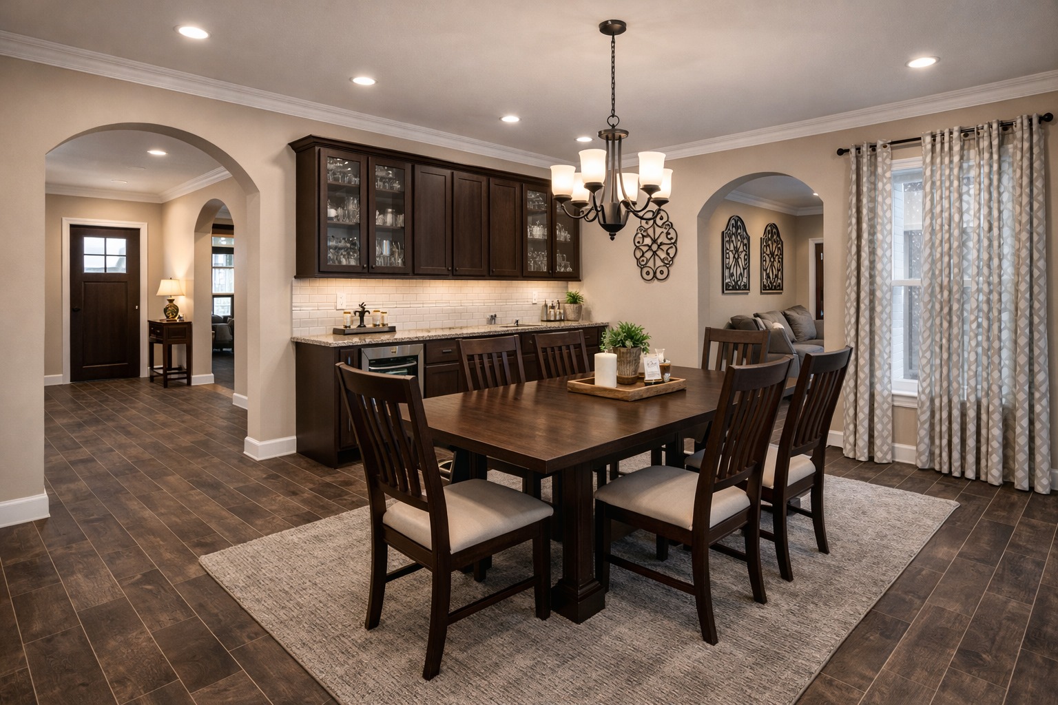 Spacious dining room with dark wood table and chairs on a textured rug. Soft lighting from a chandelier creates a warm, inviting atmosphere.