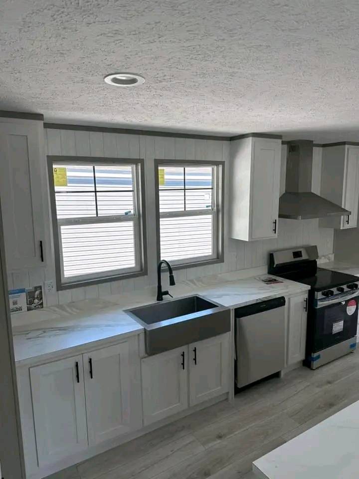 Modern kitchen with white cabinets, stainless steel appliances, and a farmhouse sink. Two windows bring in natural light, creating a bright atmosphere.