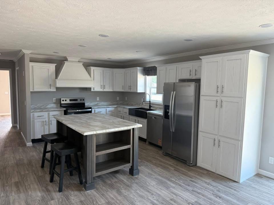 A modern kitchen with white cabinets, stainless steel appliances, and a large gray island with stools. The room is bright and has wood-style flooring.