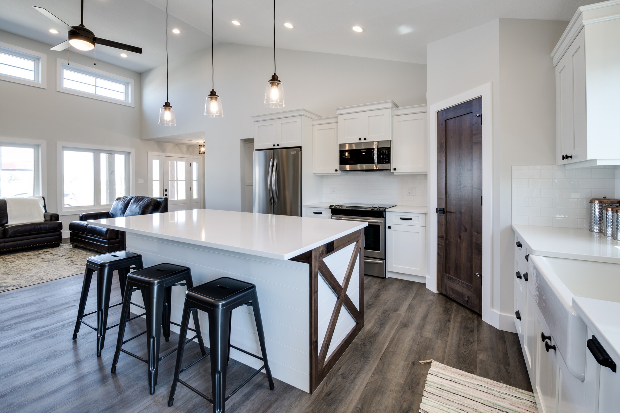 Stylish kitchen with white cabinets, dark wood accents, island with black stools, and modern appliances. Open layout and pendant lighting convey a cozy, inviting vibe.