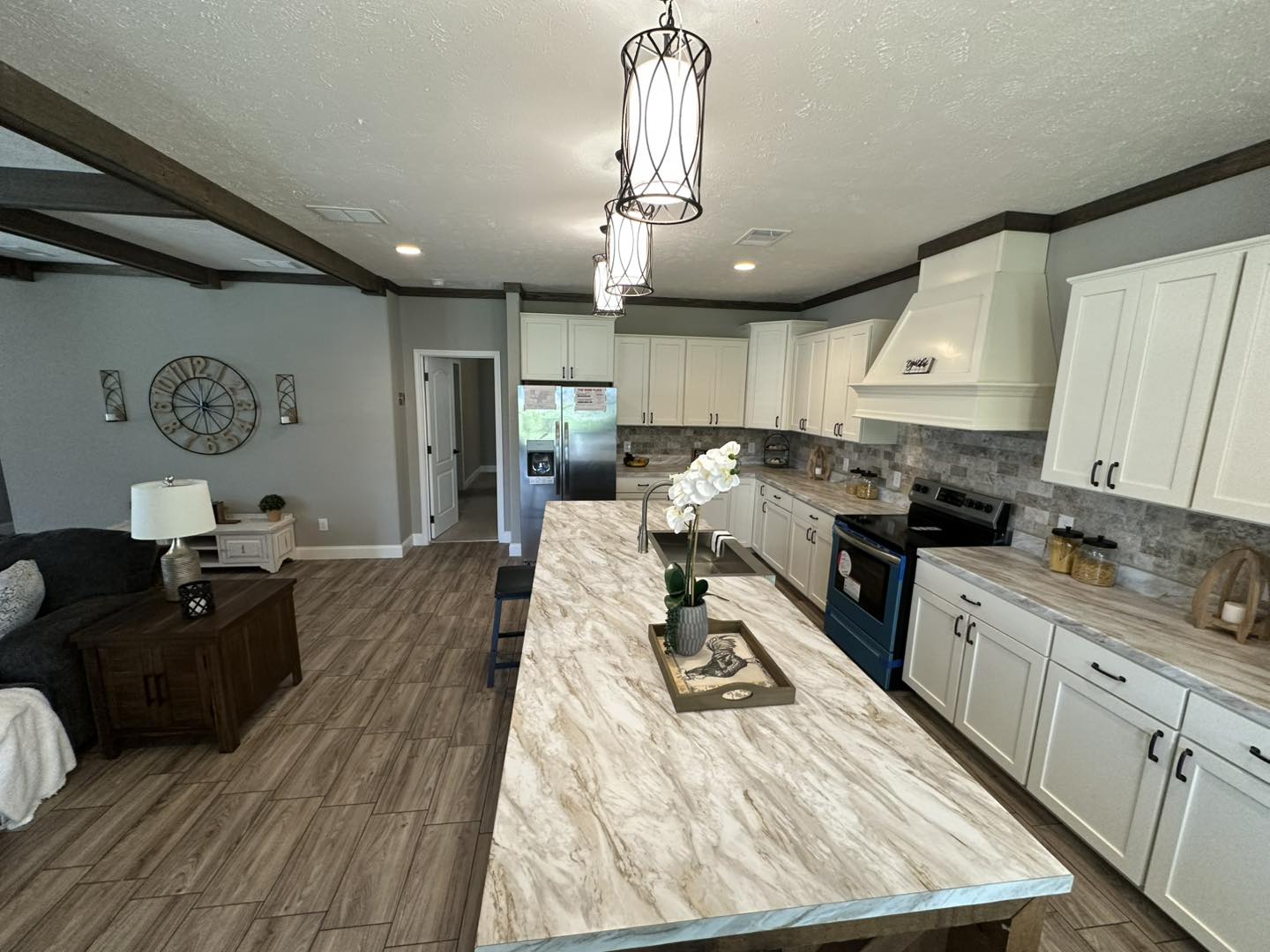 Modern kitchen with light wood flooring, marble countertops, and white cabinets. A central island features elegant lighting and an orchid. Cozy ambiance.