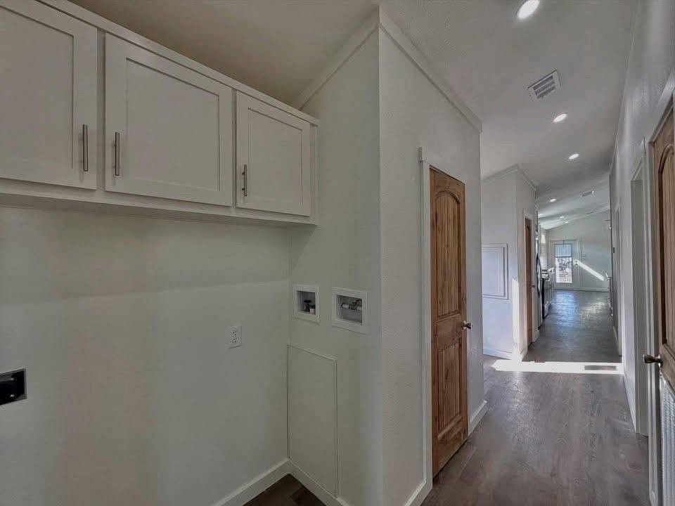 A well-lit hallway features white cabinets on the left and a natural wooden door on the right. Sunlight streams from a distant window, creating a warm, welcoming ambiance.