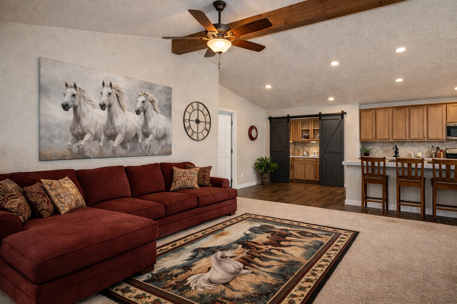 Spacious living room with a red sectional sofa, horse-themed artwork and rug, ceiling fan, and a cozy kitchen with wooden cabinets and bar stools.
