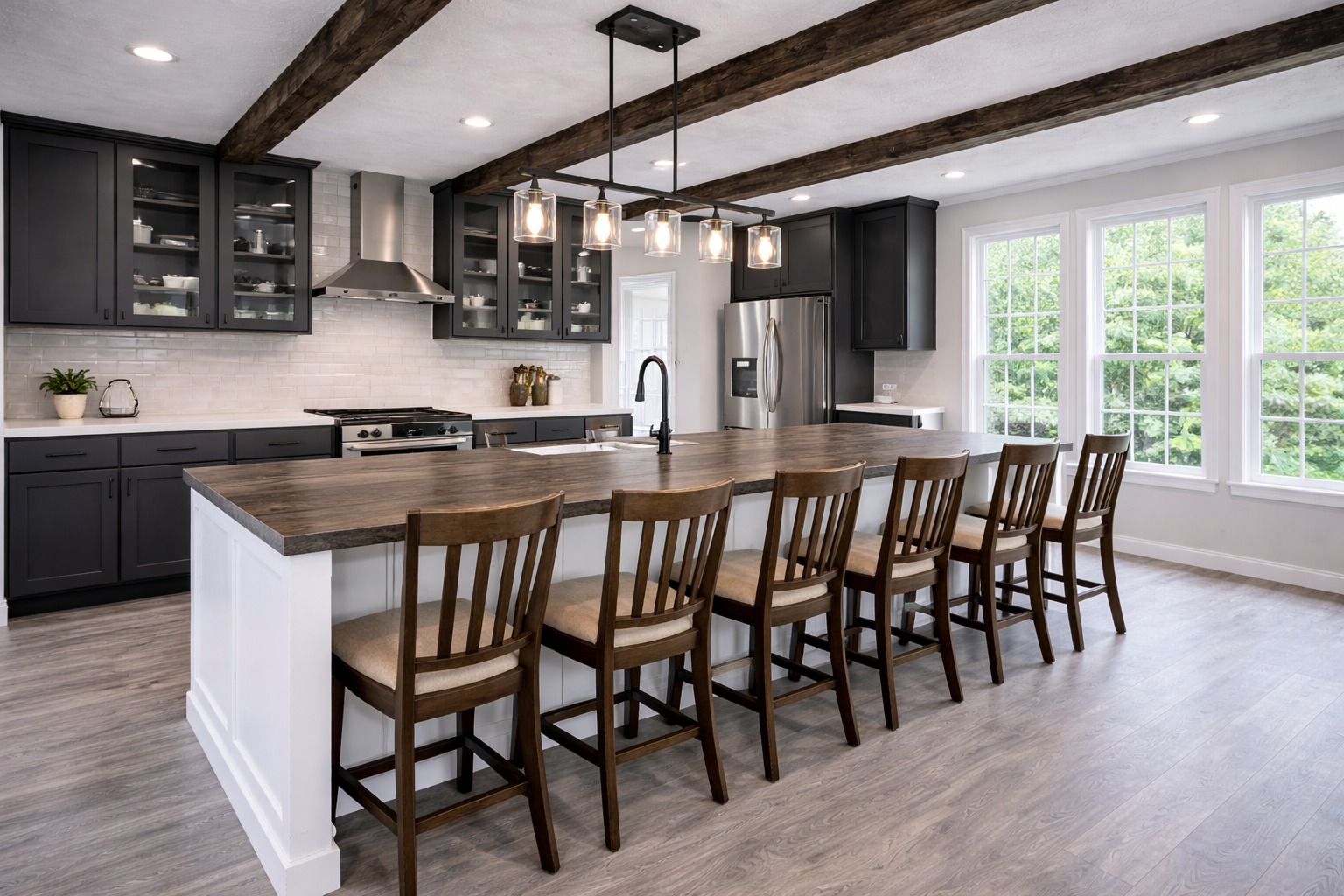 Modern kitchen with dark cabinetry, stainless steel appliances, and a large wood island topped with pendant lights. Six stools face large windows.