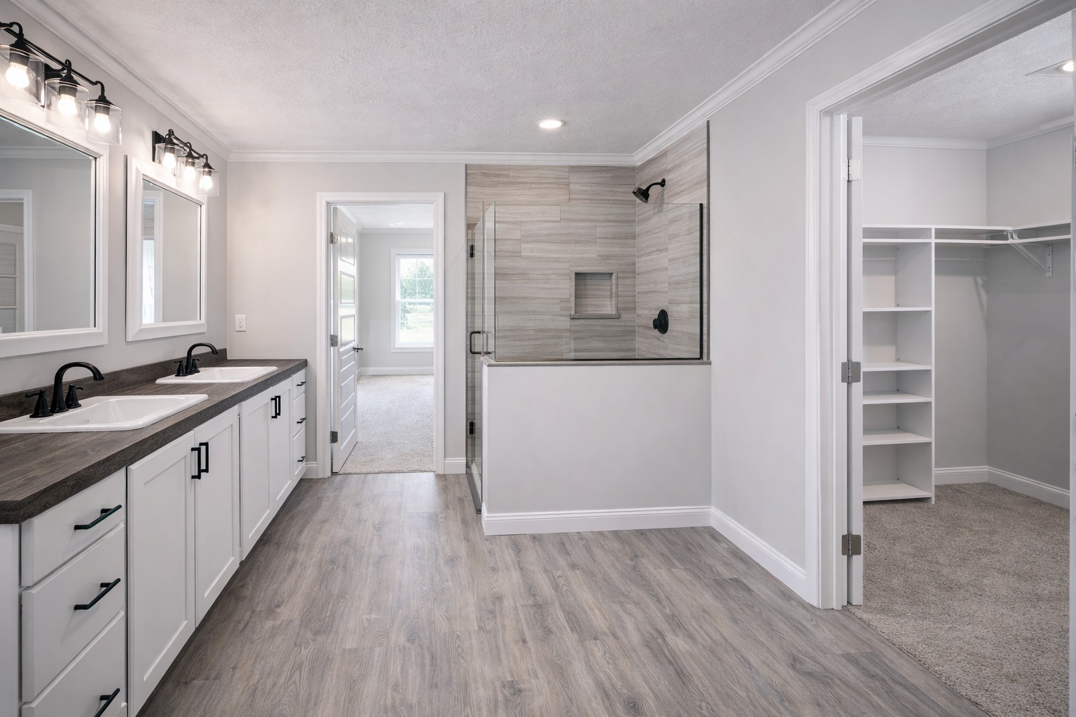 Spacious modern bathroom with dual sinks on a dark wood vanity, light gray walls, and wood-look flooring. A glass-enclosed shower is adjacent.