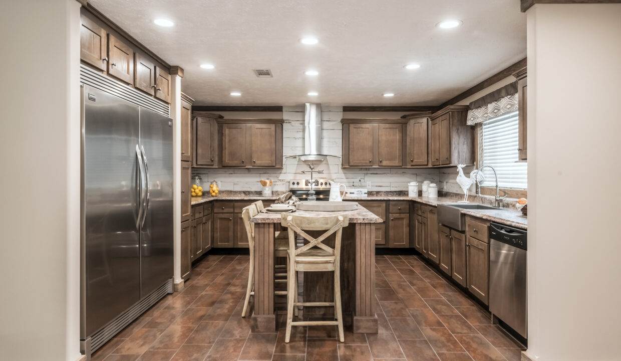 Spacious kitchen with wooden cabinets, a central island with two high chairs, stainless steel appliances, tiled floor, and warm lighting.