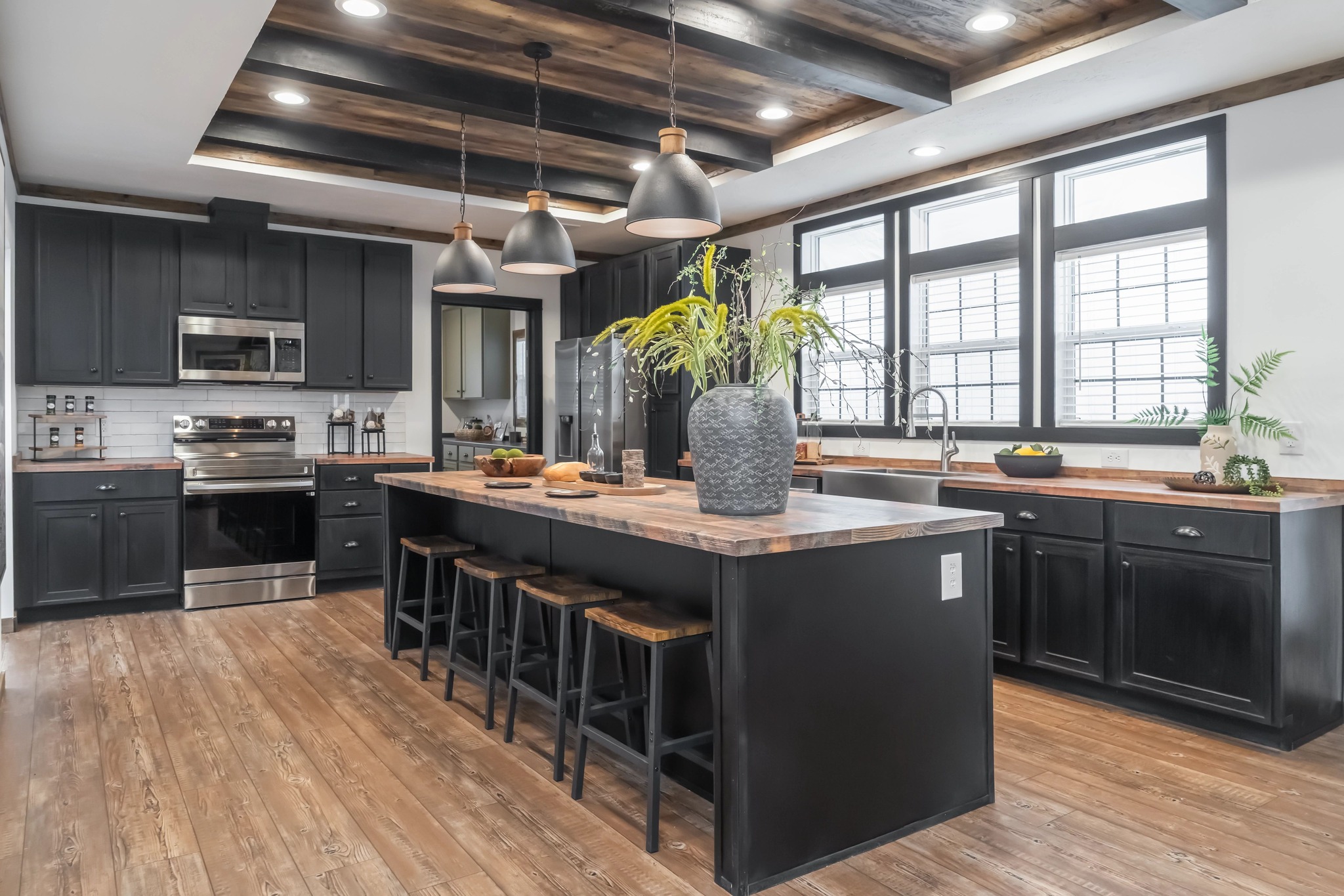 Modern kitchen with dark wood cabinets, large island with stools, and wooden countertops. Pendant lights hang above; plants add a fresh touch.
