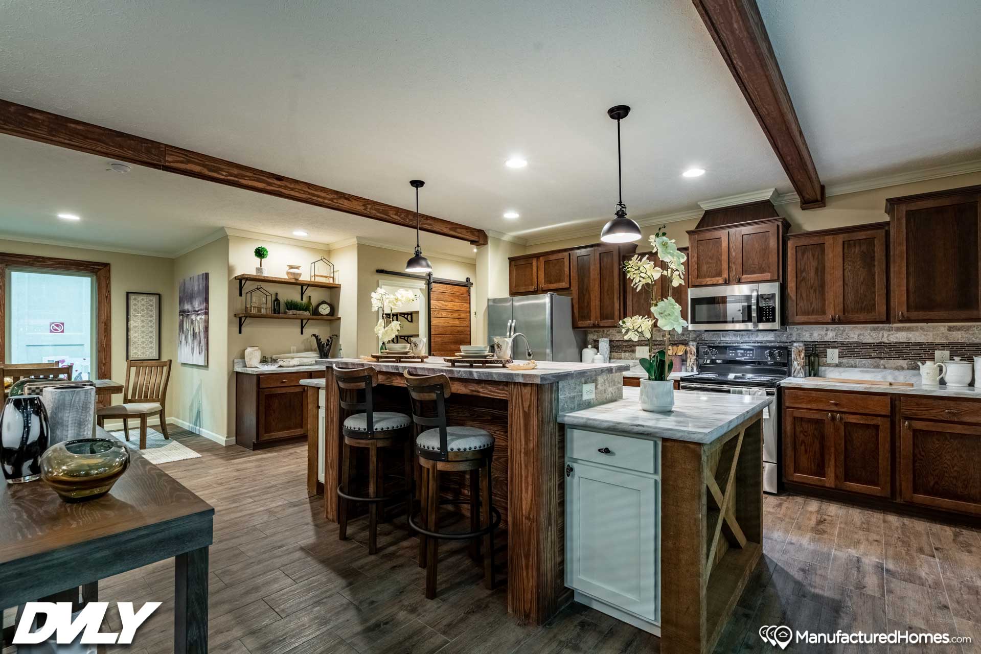 Spacious kitchen with dark wood cabinets and beams, marble countertops, and pendant lights. An island with stools and decorative orchids adds warmth.