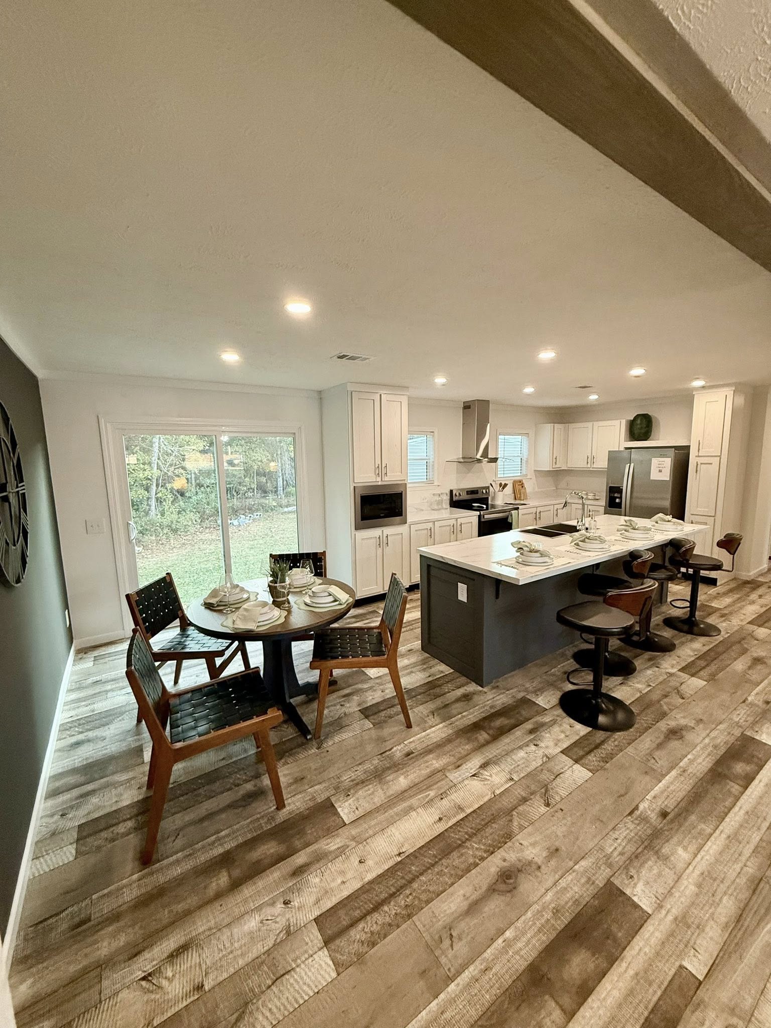 Bright, modern kitchen with wood floors, a central island with bar stools, and a round dining table set for four. Large windows bring in natural light.