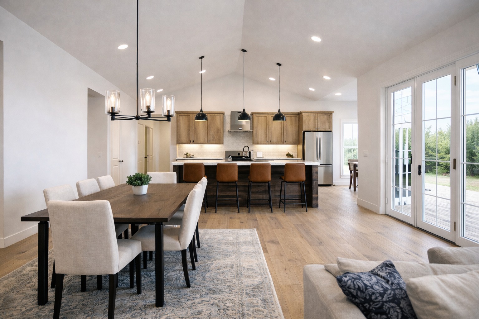 Modern open-concept kitchen and dining room. Light wood floors, elegant chandelier, large dining table, brown bar stools, and airy ambiance.