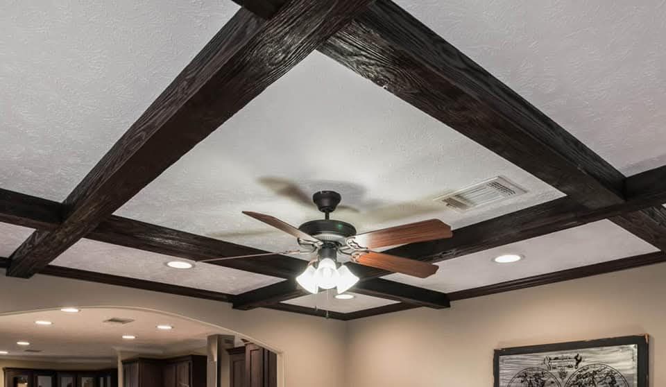 Ceiling with dark wooden beams and a central lighted fan with wooden blades. Surrounding recessed lighting adds warmth, creating an inviting ambiance.