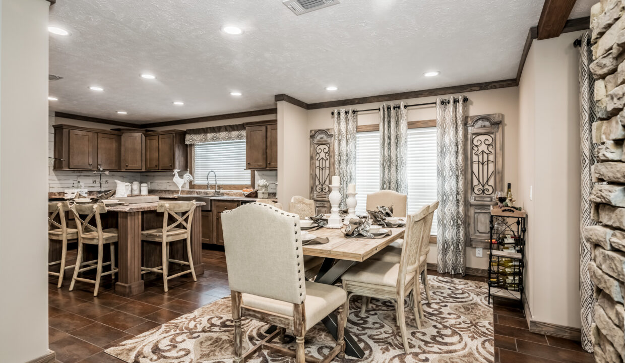 A cozy dining area with a wooden table set for six, cream chairs, ornate rug, and decorative curtains. Rustic kitchen with wooden cabinets in the background.