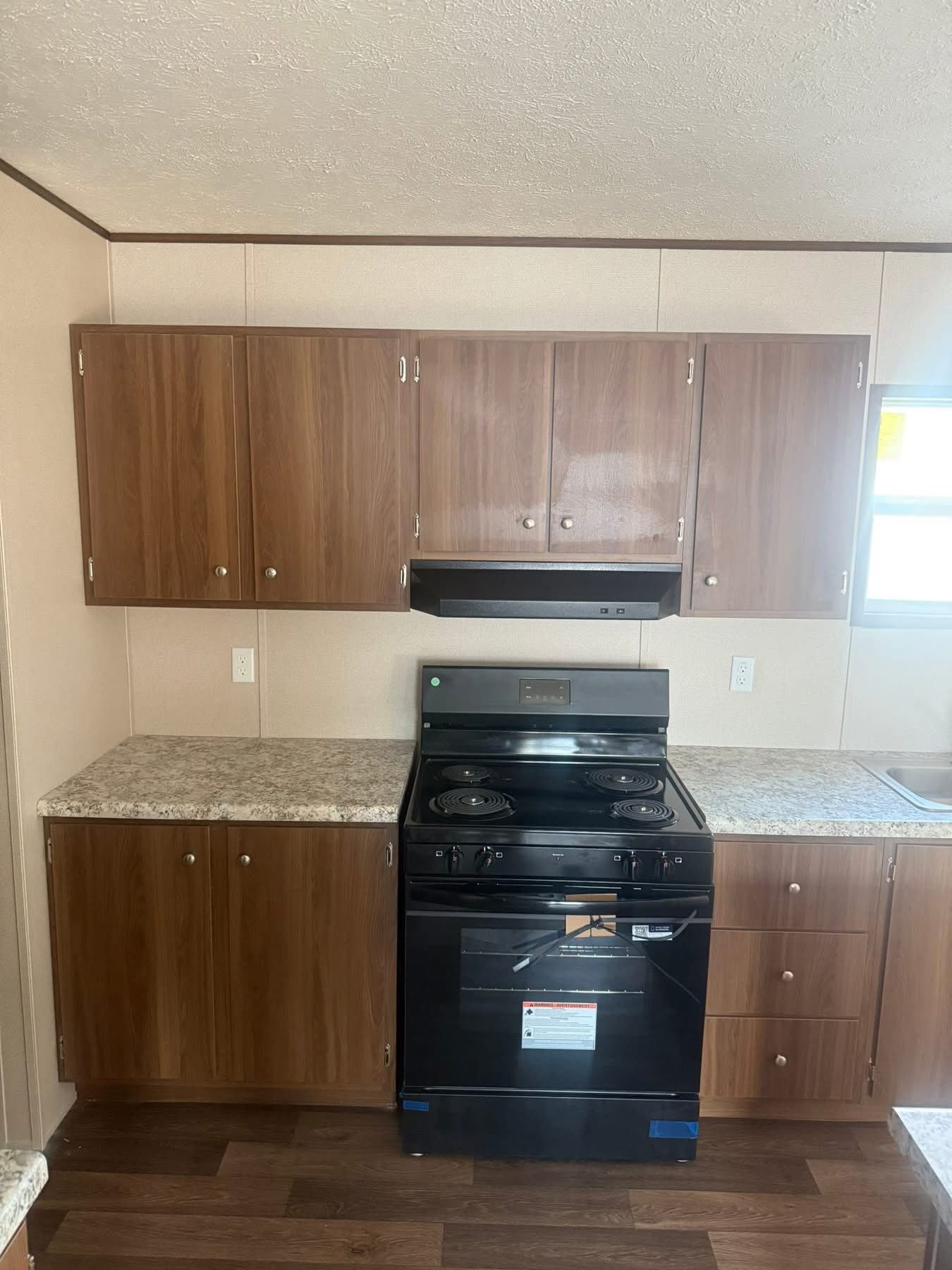 Compact kitchen with light brown cabinets, a black stove, and speckled countertops. Cozy, well-organized space with a warm, inviting atmosphere.