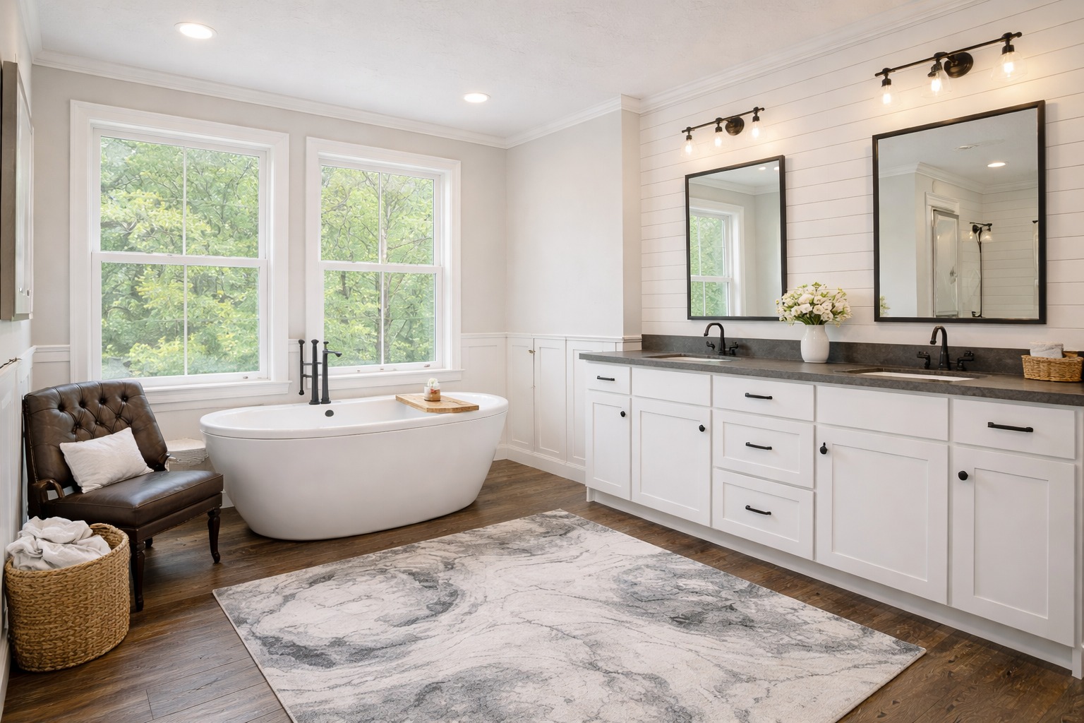 Spacious bathroom with a freestanding tub by large windows, a brown leather chair, basket, white double-sink vanity, and a plush rug, exuding elegance.