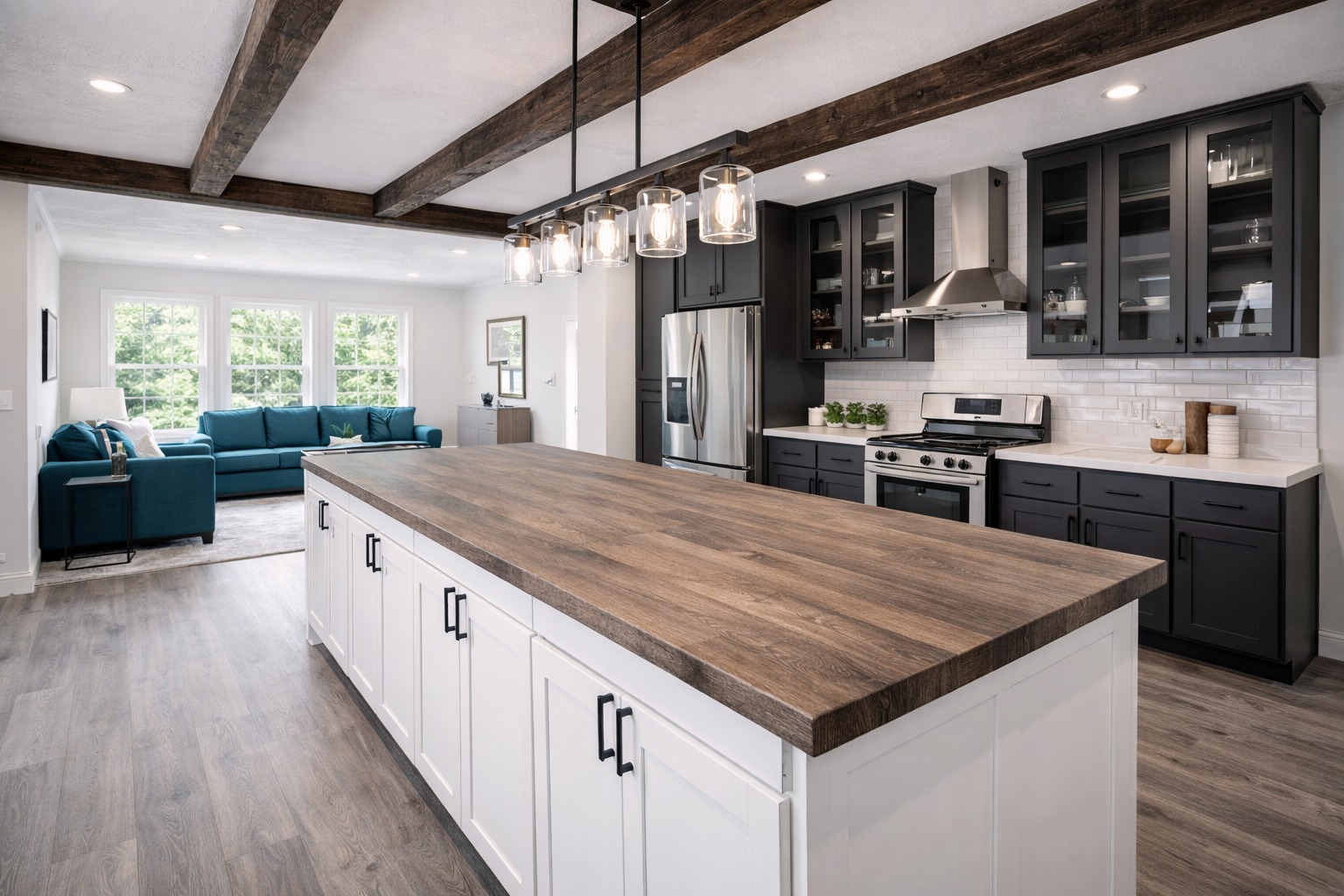 Modern kitchen with a large wooden island, white base cabinets, dark upper cabinets, stainless steel appliances, and an adjacent cozy living room.