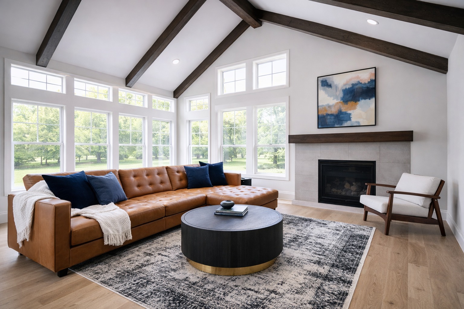 Spacious living room with a brown leather sectional, navy cushions, and a cozy rug. Large windows showcase a green landscape, creating a serene ambiance.