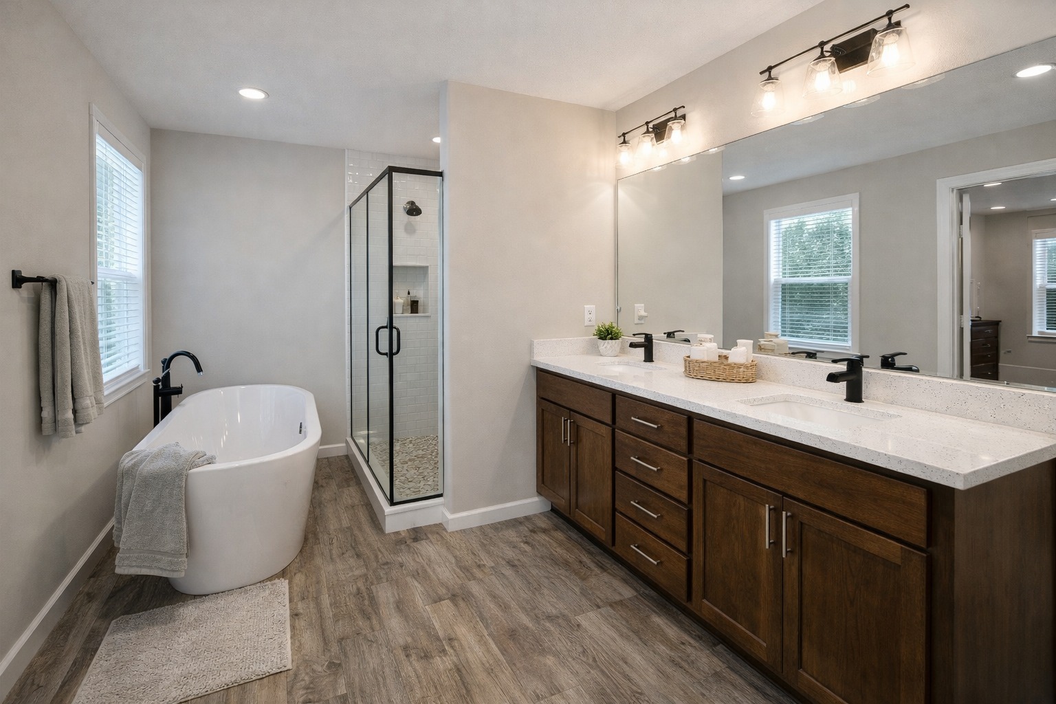 Modern bathroom with wood flooring, featuring a freestanding bathtub, glass shower, and double sink vanity with dark wood cabinets and bright lighting.