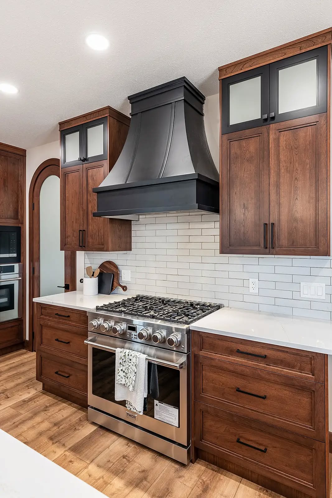 Modern kitchen with white subway tile backsplash, dark wood cabinets, and stainless steel oven. A large black range hood adds a sophisticated touch.