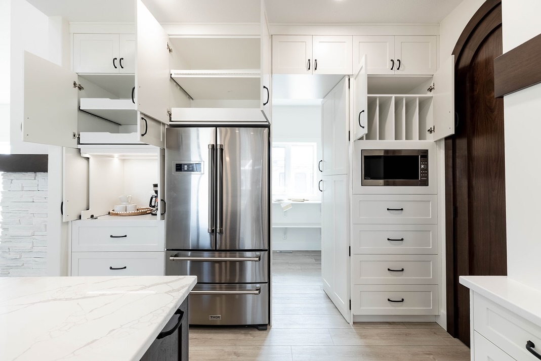 Modern kitchen with open white cabinets showing spacious storage, stainless steel fridge, and microwave. Bright, organized, and minimalist.