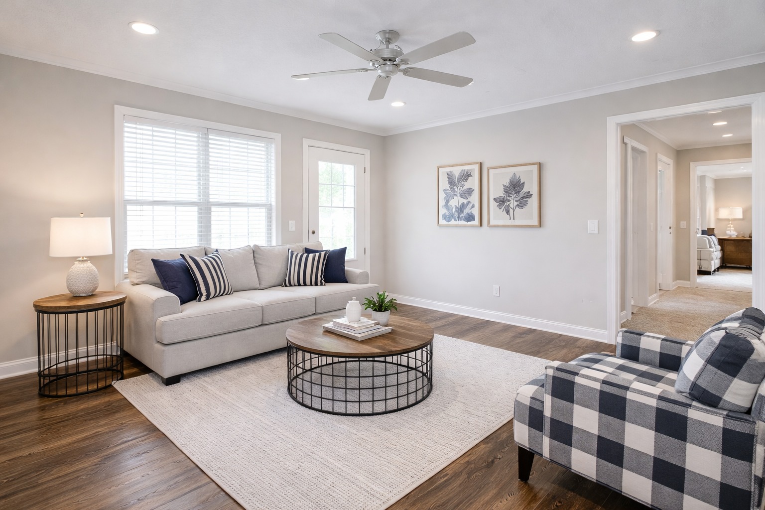 Stylish, cozy living room with neutral tones. Features a gray sofa, checkered armchair, wooden coffee table, and botanical wall art. Warm, inviting vibe.