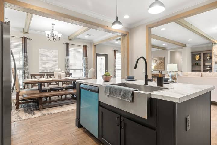 Spacious modern kitchen dining area with wooden beams, a farmhouse sink, pendant lighting, and sleek black cabinets. Cozy, inviting ambiance.