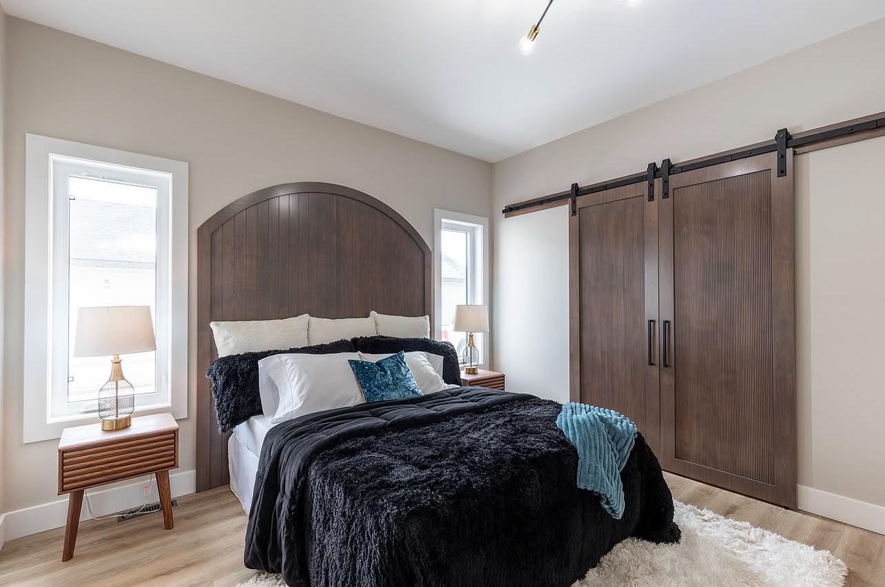 Modern bedroom with a soft color scheme. Features a bed with dark wood headboard, plush black bedding, and teal accents. Barn doors and side lamps add elegance.