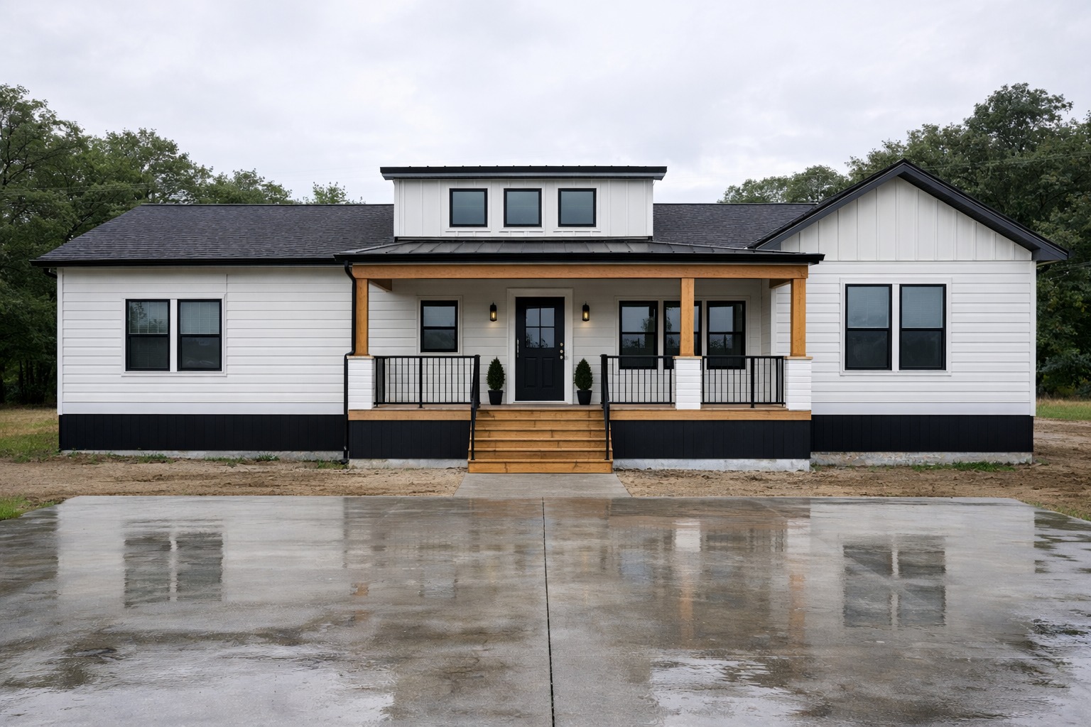 Modern white ranch-style house with black accents, a covered porch, wooden columns, and large windows. Reflective wet driveway and overcast sky.