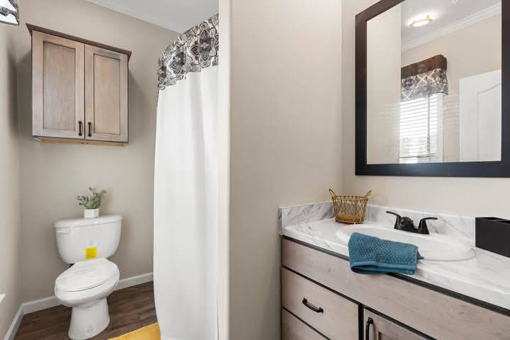 Modern bathroom with beige walls, a wooden vanity with a marble sink, a mirror, shower curtain, and a toilet. A cozy, clean, and inviting space.