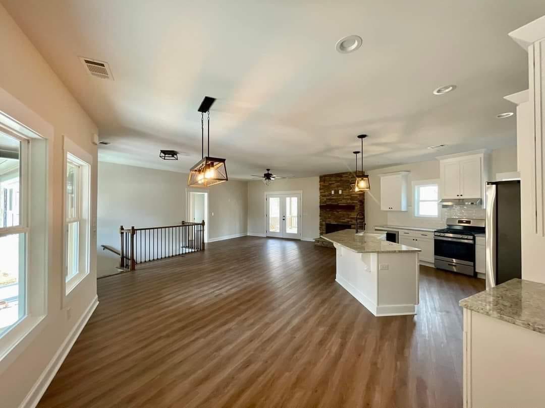 Spacious open-plan kitchen and living area with hardwood floors, pendant lighting, white cabinetry, and a stone fireplace, creating a warm, inviting atmosphere.