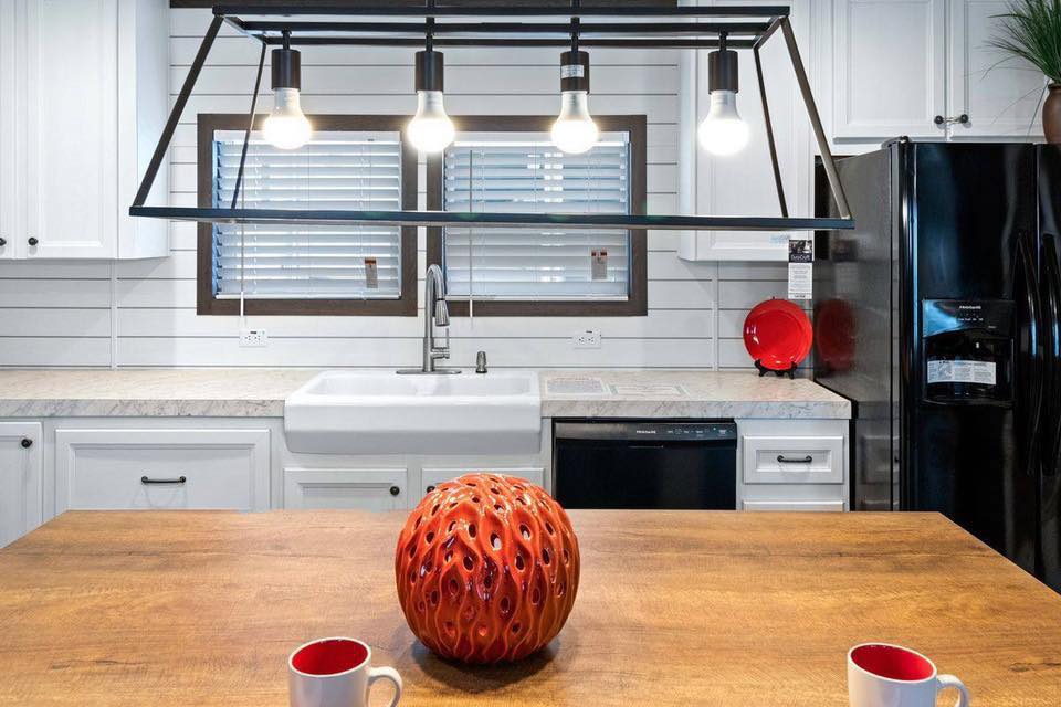 Modern kitchen with white cabinets and a farmhouse sink. A wooden island features a decorative red vase. Three pendant lights hang above, creating a cozy atmosphere.