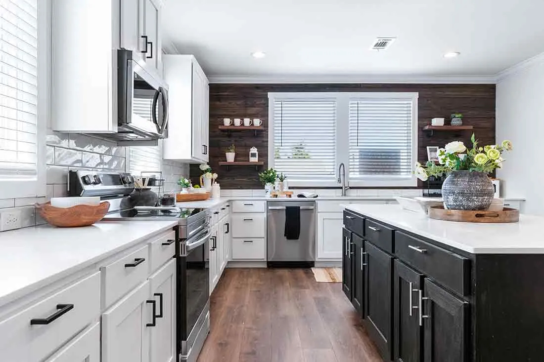 Modern kitchen with white and black cabinets, stainless steel appliances, wood floors, and a dark accent wall. Fresh flowers on the island add a bright touch.