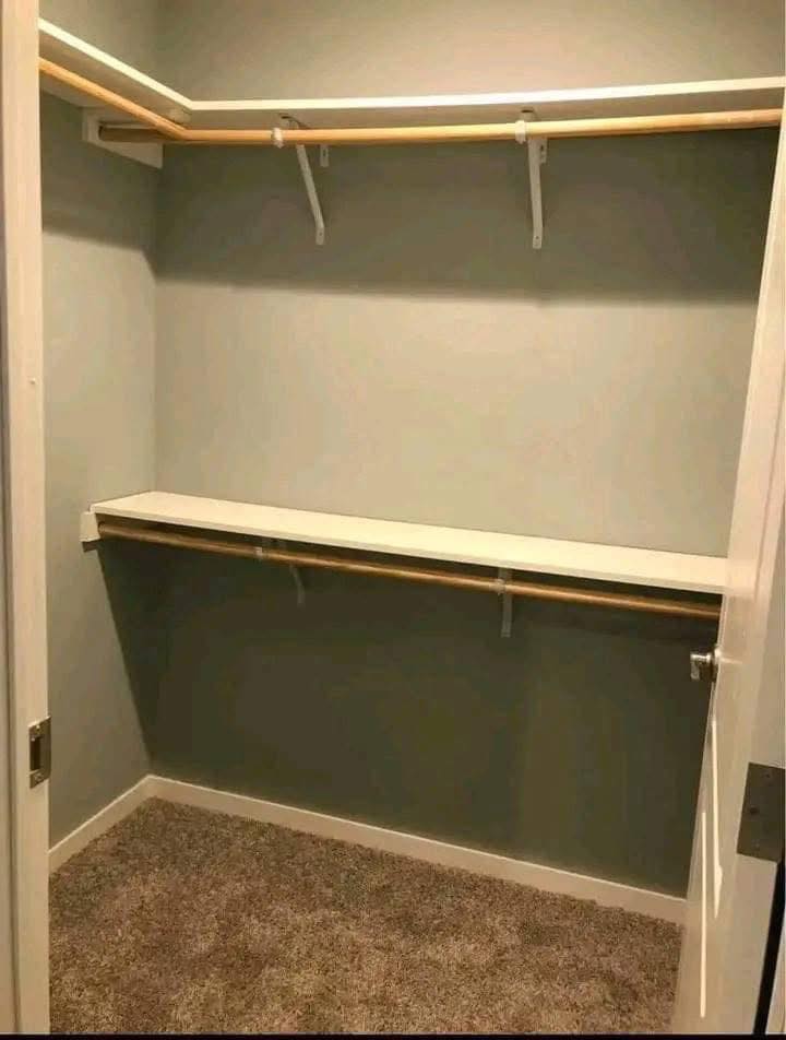 Empty walk-in closet with gray walls, beige carpet, and two wooden clothing rods with white shelves. The space feels clean and minimalist.